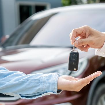 Person handing over car keys to another in front of a vehicle.