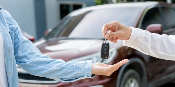 Person handing over car keys to another in front of a vehicle.