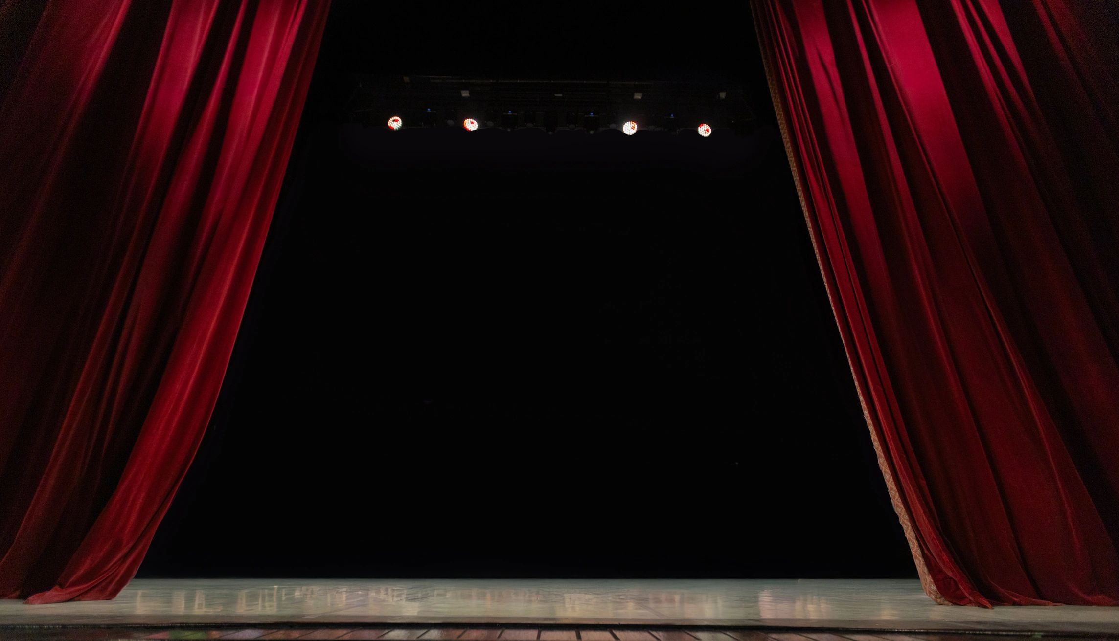 Empty stage framed by red theater curtains and overhead lights.