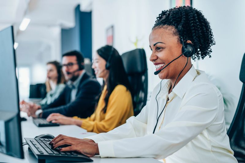 Shot of call center operators working in the office. Call center agent working with her colleagues in modern office. Smiling beautiful businesswoman working in call center.