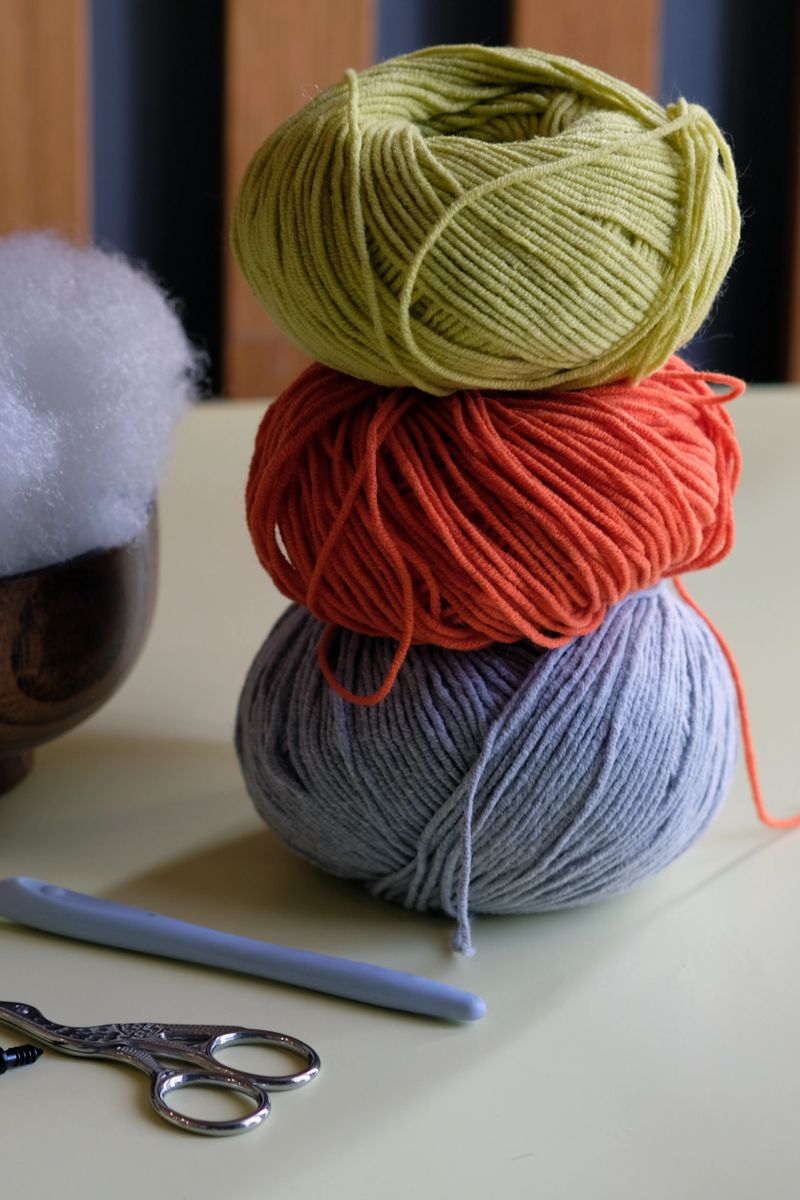 Colorful yarn, stuffing, and tools are arranged on a table in a warm, inviting environment, signaling a fun crafting session. This setup encourages creativity and hands-on enjoyment.
