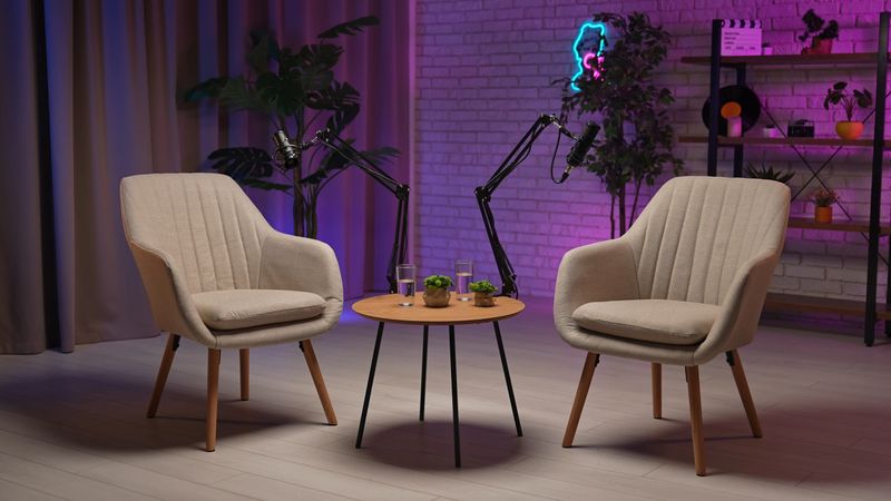 Two stylish chairs await an engaging dialogue in a contemporary podcast studio. The inviting atmosphere is enhanced by soft lighting, a recording setup, and personal touches, perfect for storytelling.