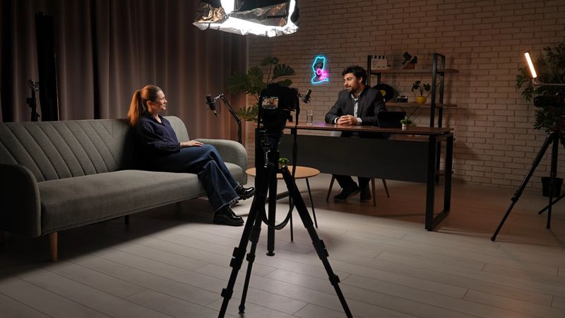 Backstage. Two guests engage in a dynamic dialogue within a creatively designed podcast studio, equipped with microphones and lighting. The atmosphere is filled with excitement and storytelling potential.