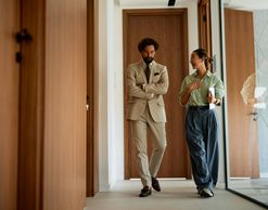 Two professionals walking and chatting in a modern office hallway.