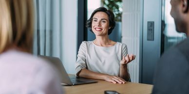 Woman in a meeting smiling and gesturing while talking to two colleagues.