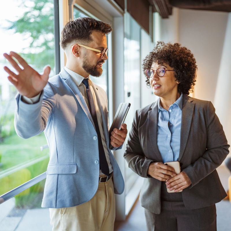 Two happy diverse business team people, adult businessman and aged woman executive work and talk in corporate office