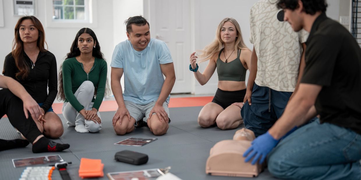 Group learning CPR with a man demonstrating on a mannequin.