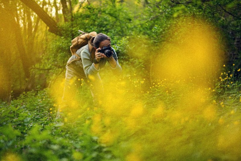 Woman explorer wearing smartwatch is taking pictures with old film camera in lush green rainforest, connecting retro tech feeling & contemporary art photography