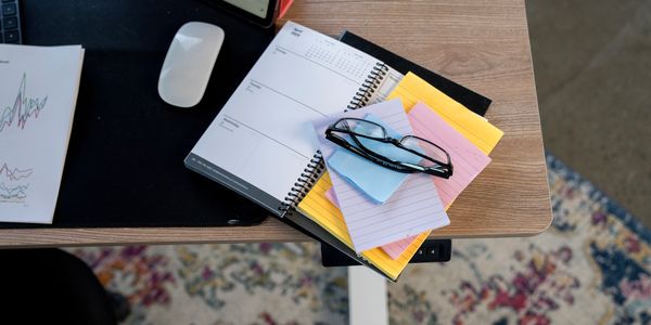 Desk with planner, sticky notes, glasses, and mouse.