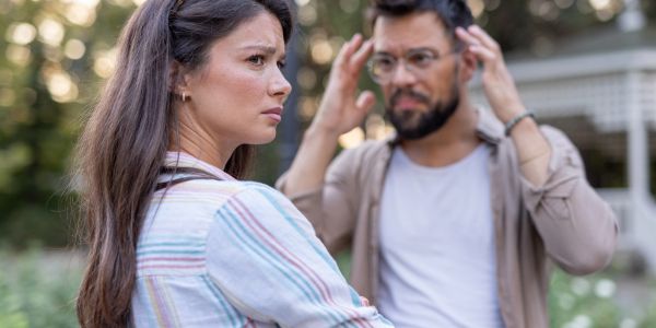 A woman looks upset while a man gestures in frustration behind her.