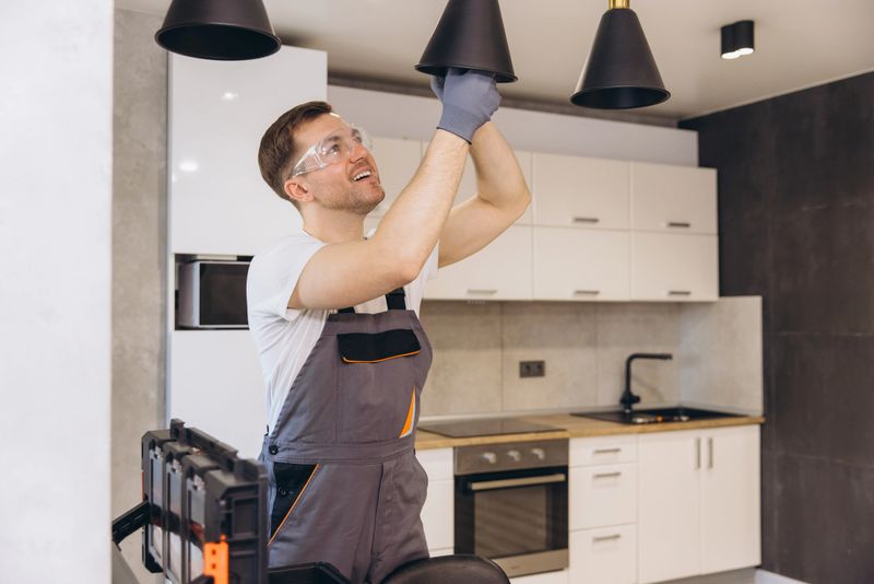 Electrician working on pendant lamp installation in a modern kitchen, ensuring proper lighting and functionality