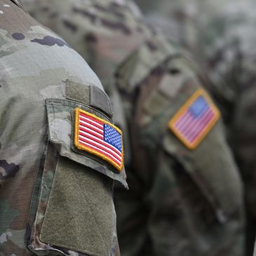 Close-up of soldiers' sleeves with American flag patches on camouflage uniforms.