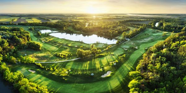 Sunset over a lush golf course surrounded by trees and water.