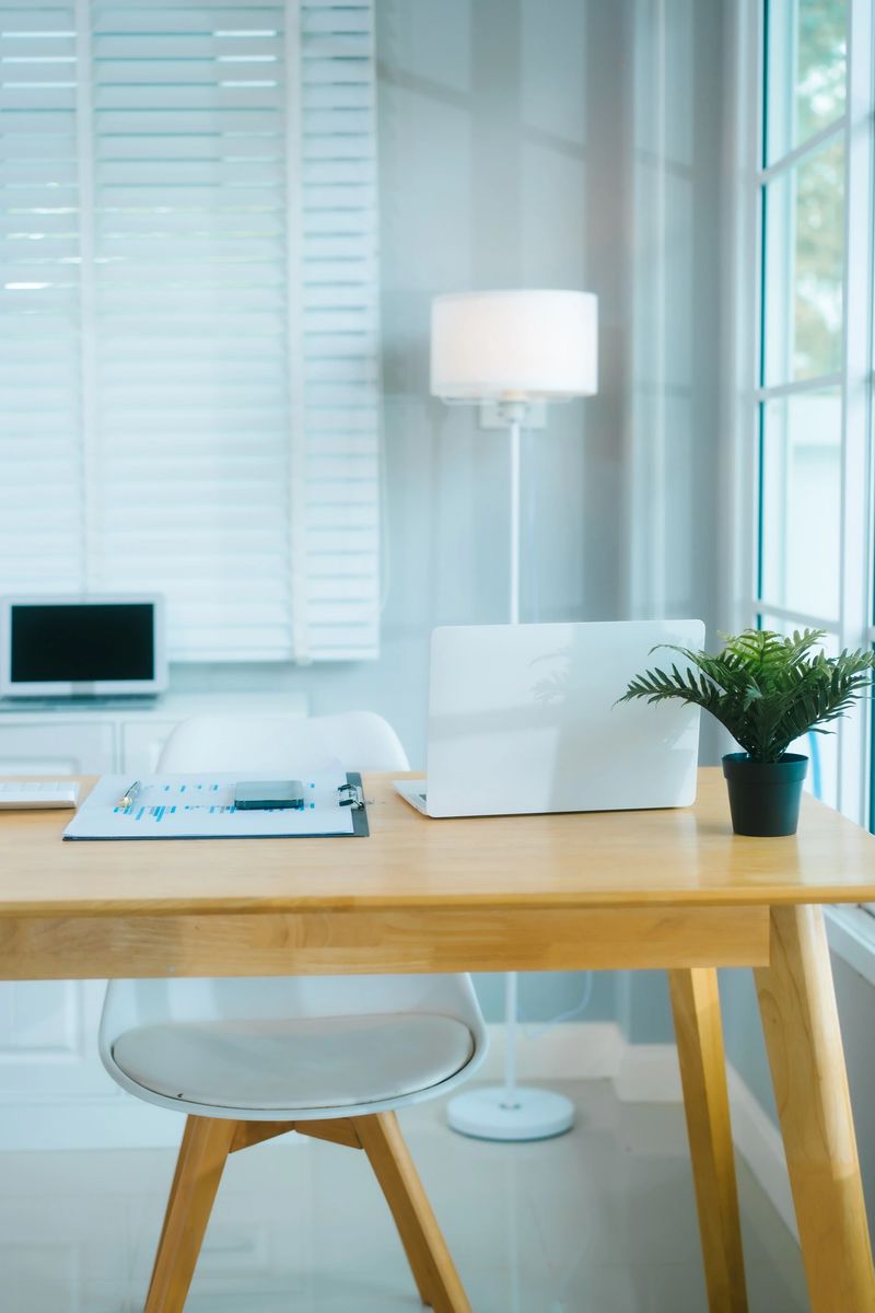 A clean, modern home office features a laptop, plant, and organized desk, ready for productive work in a bright, minimalist setting.
