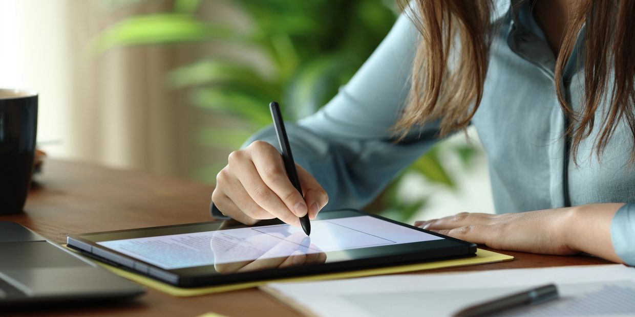 Person using a stylus to write on a tablet at a desk.