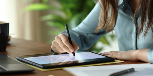 Person using a stylus to write on a tablet at a desk.