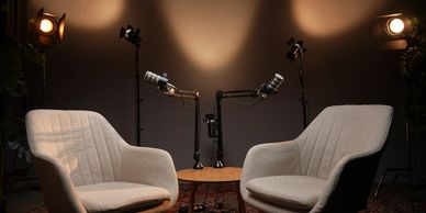 Two white armchairs with microphones set up for a podcast recording.
