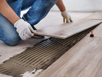 Worker installing wood-look tiles on the floor with adhesive.