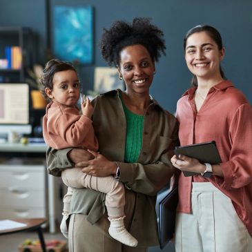 Two women and a toddler smiling indoors.