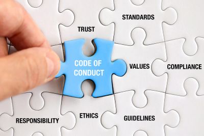 Hand placing a puzzle piece labeled 'Code of Conduct' among pieces with related terms.