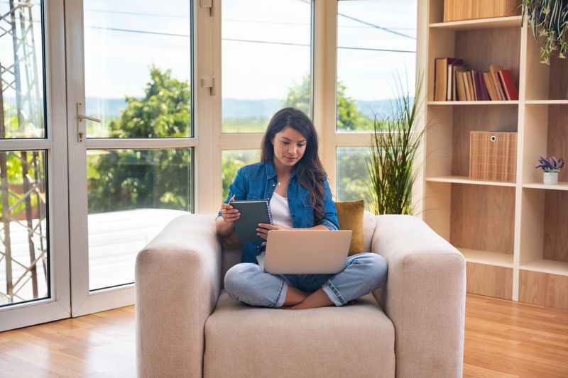 Young home-based online therapist in virtual counseling session, focused mental health professional listening to client on video call taking notes offering support and empathy in calm domestic setting