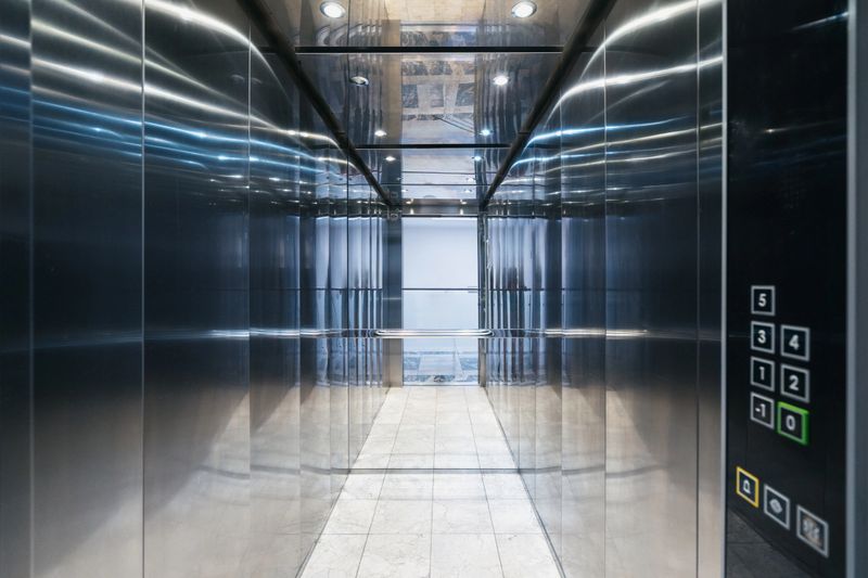 Elevator interior with mirror. Residential building with empty lift cabin inside. Sleek metal walls reflect light, creating an open space. The control panel displays floor numbers
