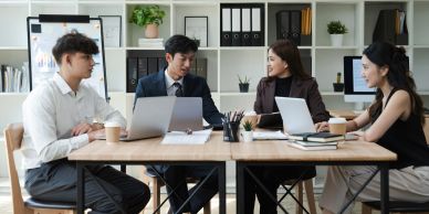Four colleagues discussing work at a table with laptops.