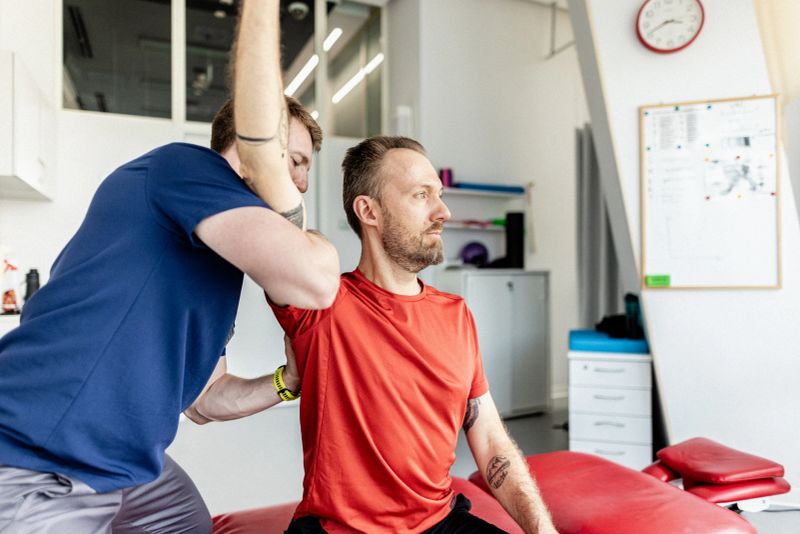 A therapist assists a patient in a clinical setting, guiding him through a precise rehabilitation exercise to improve mobility and strength. The setting is bright and supportive, emphasizing professional care.