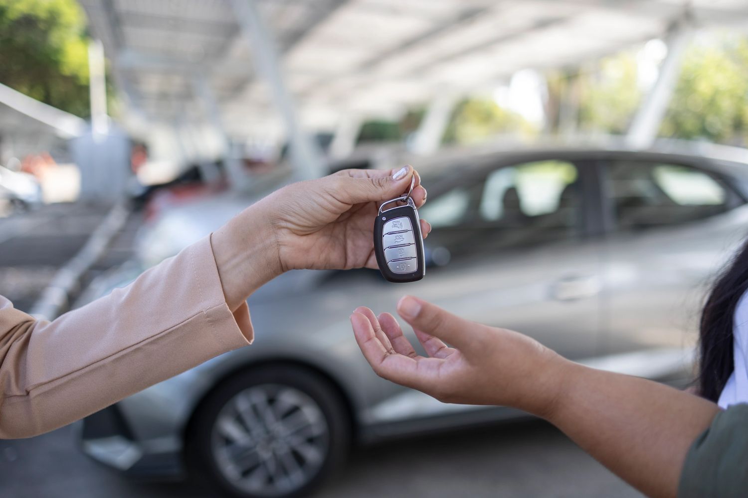 Person handing over car keys to another by a parked car.