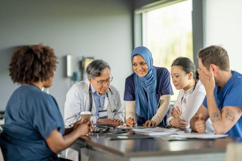 Healthcare professionals, including doctors and nurses, engage in a collaborative discussion in a modern medical environment, showcasing teamwork and diverse staff focusing on joint decision-making and patient care.