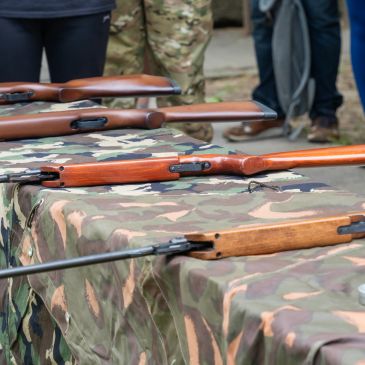 Rifles lined up on a camo-covered table.