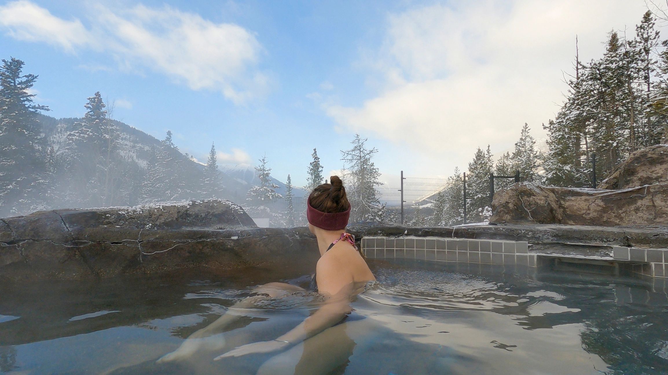 Person relaxing in an outdoor hot pool surrounded by snow-covered Rocky Mountains  Alberta, Canada.
