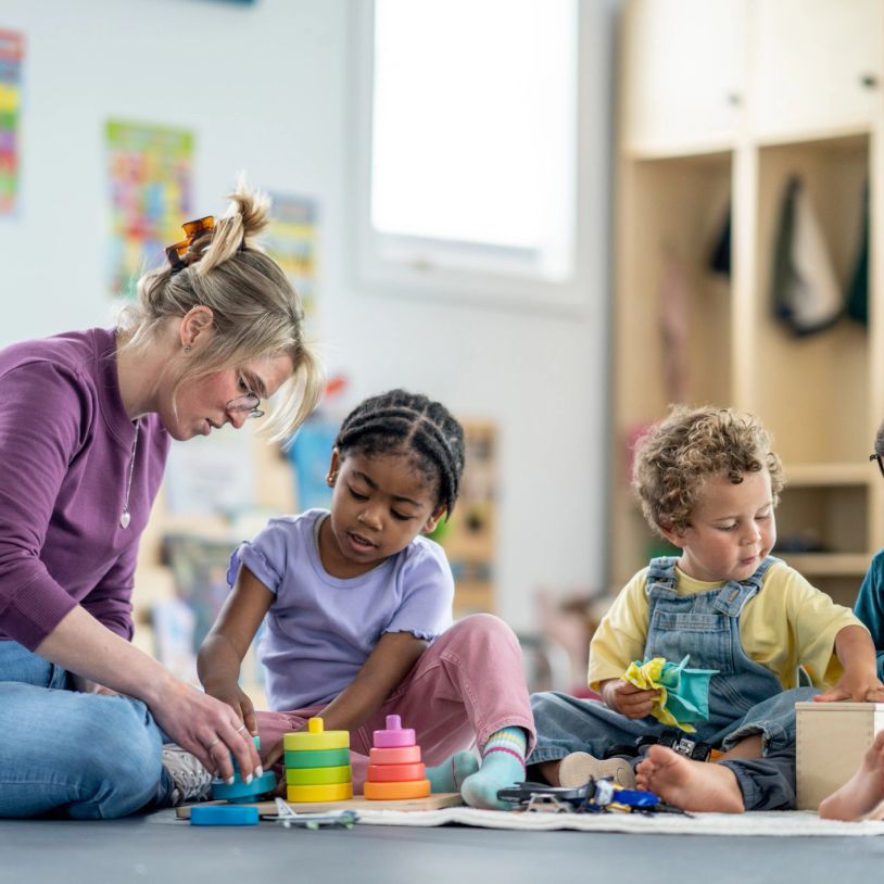 Teacher guiding children playing with colorful stacking toys in a classroom.