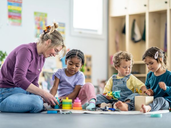 Teacher and children playing with colorful educational toys on the floor.