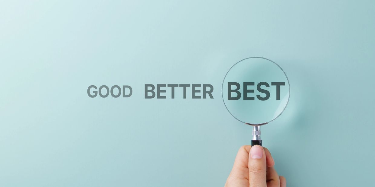 Hand holding a magnifying glass emphasizing the word BEST over GOOD and BETTER.