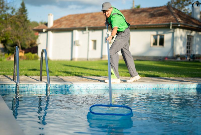Male worker swimming pools maintainer is hired to clean out a pool in a private house.