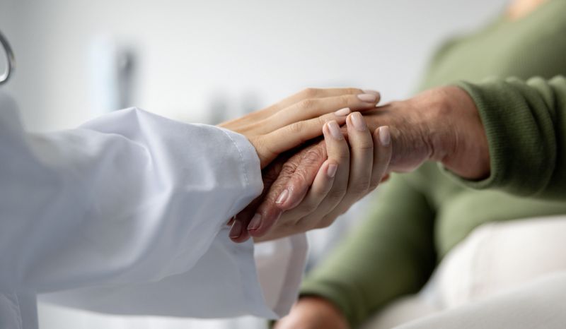 Close-up on a doctor holding the hand of a senior patient at the hospital while consoling her