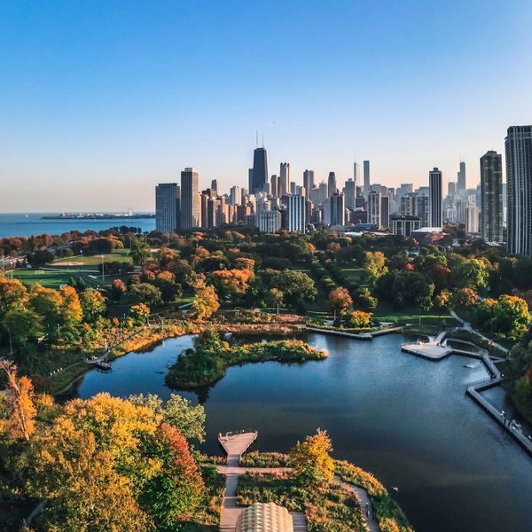 A vibrant city skyline with a lush park and lake in the foreground during autumn.