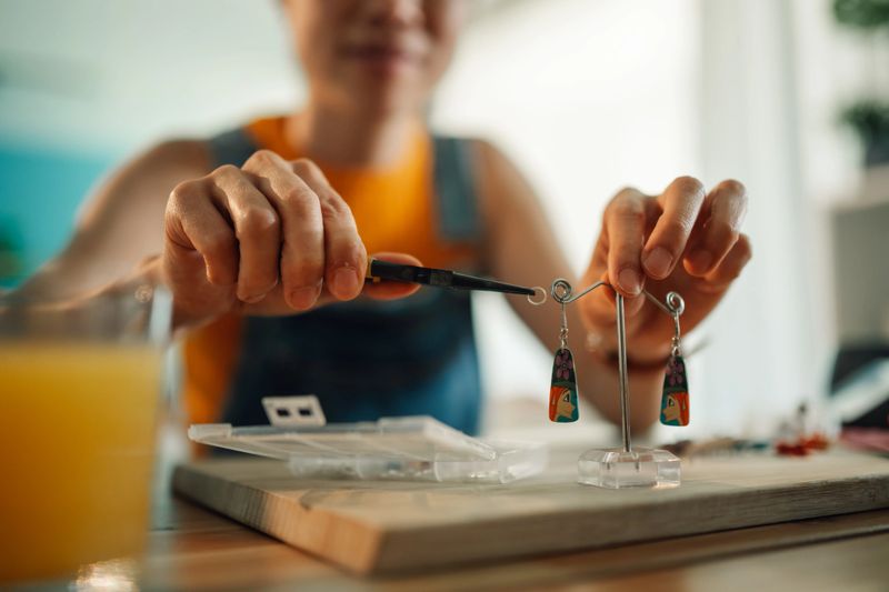 Close-up of artisan using pliers, crafting unique earrings with vibrant colorful designs in their workshop