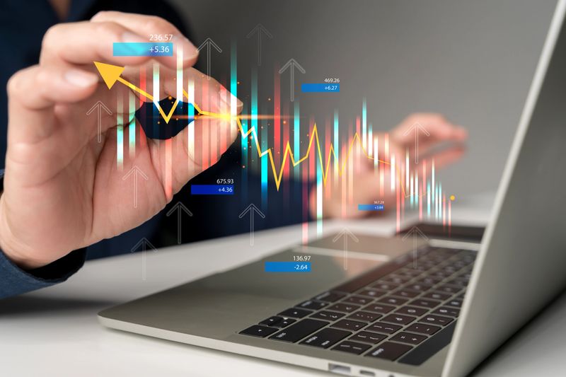 Business hand interacting with stock market graph, candlestick chart over laptop screen, symbolizing financial trading, economic data analytics, investment strategy, and digital stock exchange tools.