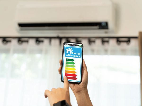 Person checking energy efficiency on a phone below an air conditioner.