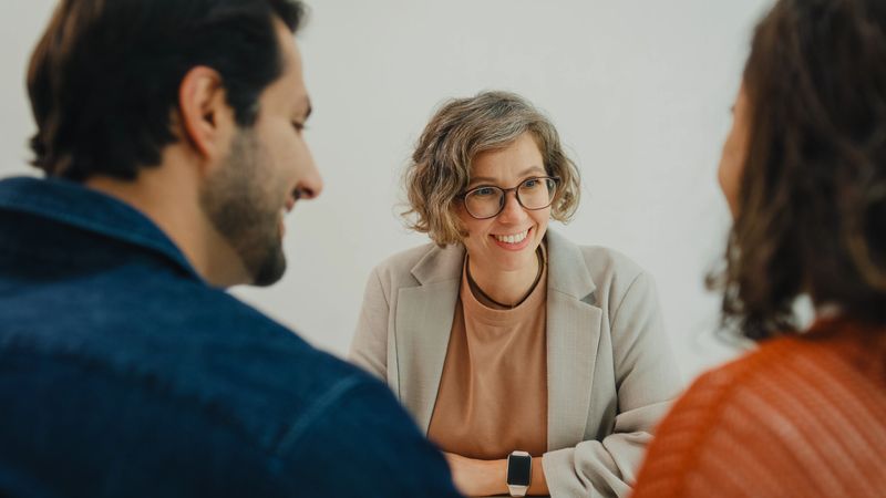 Financial advisor using digital tablet discussing about life insurance and domestic finances with young couple in living room at home. Financial planning and modern lifestyles concept.