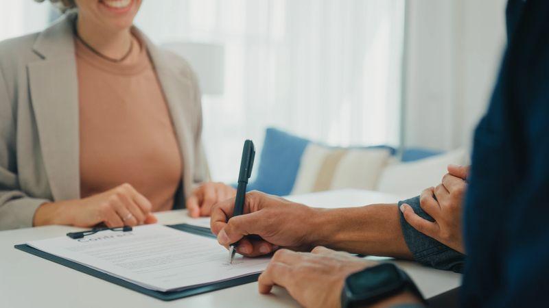 Close-up of client young couple signing a contract financial agreement meeting with financial advisor in living room at home. Financial planning and modern lifestyles concept.
