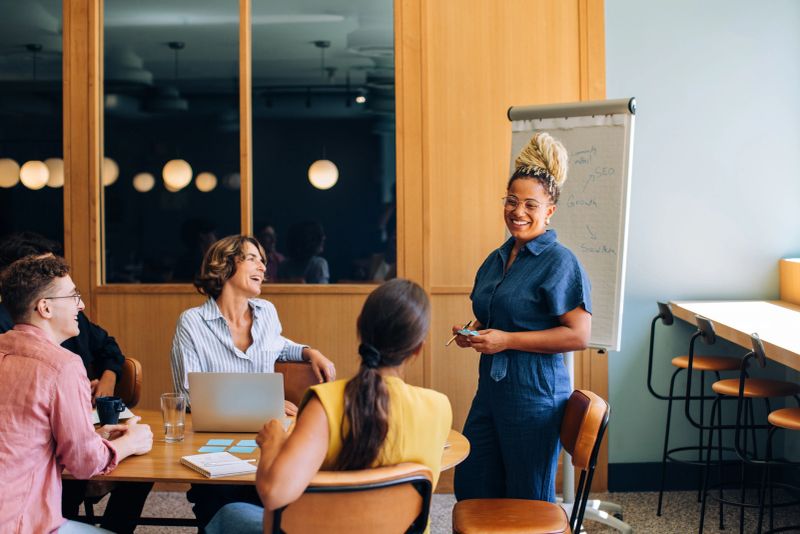 A group of diverse professionals engages in a collaborative meeting, discussing ideas and strategies, in a contemporary office environment featuring a whiteboard and warm, natural lighting.