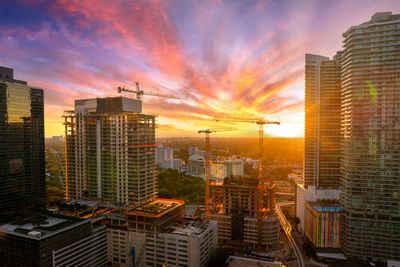 City skyline with cranes at sunset under a vibrant sky.