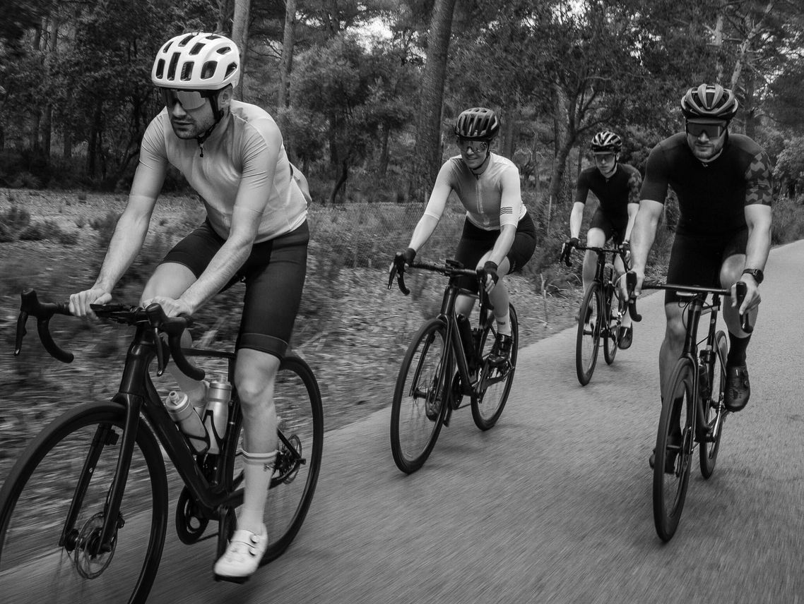 Four cyclists riding on a forest road in black and white.