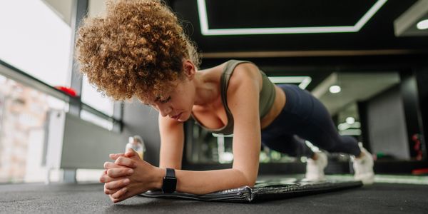 Woman with curly hair doing a plank exercise in a gym.