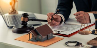 Legal professional reviewing a contract agreement with house model and gavel on desk.