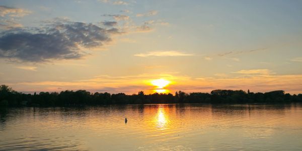A serene sunset over a calm lake with reflections on the water.