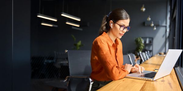 A woman in an orange shirt working on a laptop in a modern office.